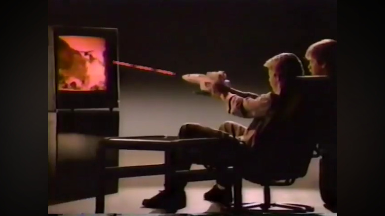 A child pointing a toy shaped like a spaceship at a TV with red lines coming out to indicate he's playing a shooting game