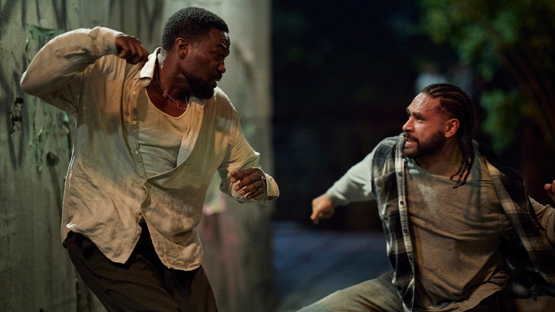 John Creasy throws a haymaker at a crouching assailant in a dark, graffitied back alley.