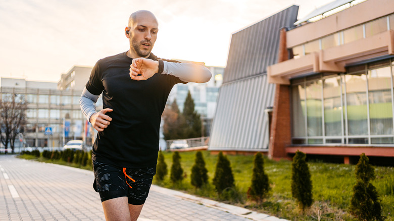 a man running on a sidewalk and looking at his smartwatch