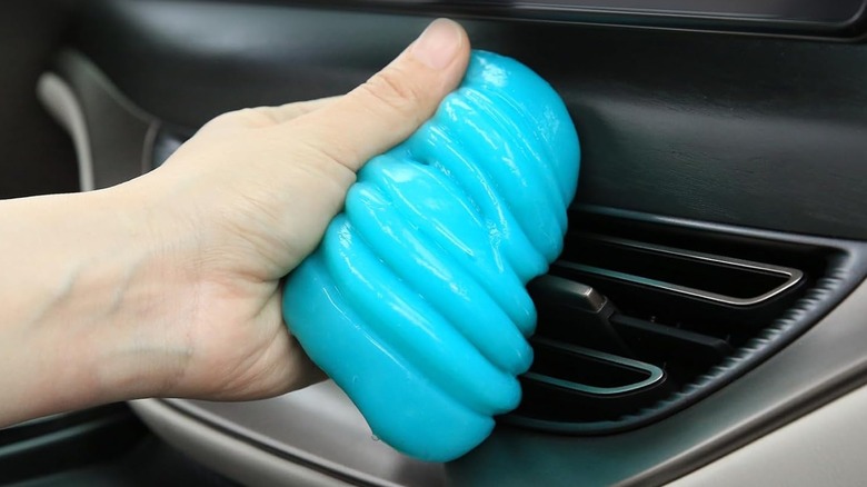 An Amazon promotional photo for the PULIDIKI Car Cleaning Putty, the image shows the bright blue putty in an individual's left hand as they are pull it from the interior of a vehicle