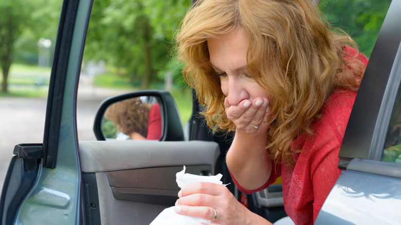 woman suffering from motion sickness, stopped leaning out of car door with bag