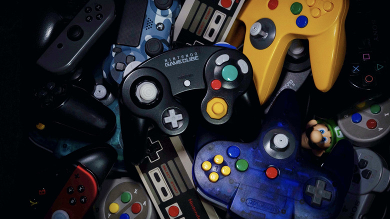 A pile of gaming console controllers with a GameCube controller on top.