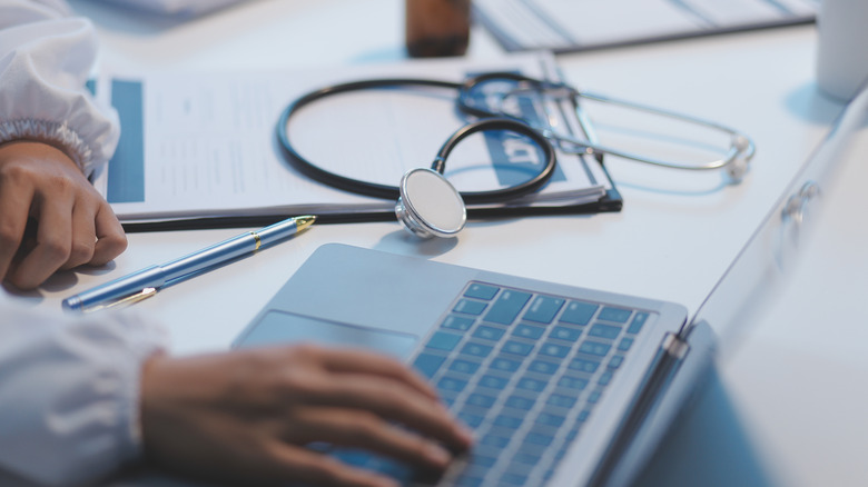 a doctor's laptop and instruments by a medical notepad