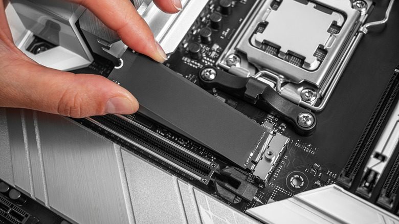 A person holding an SSD as it is being placed onto a motherboard