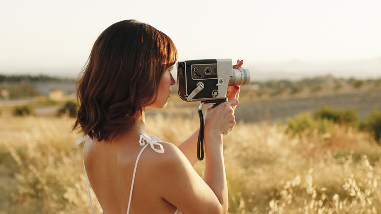 Young woman in a field looking through the viewfinder of a vintage camera.
