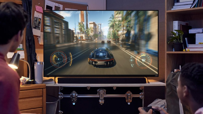 Two kids are playing a video game on a VIZIO Full HD TV, the TV sits on top of a chest and is next to a bookshelf and desk