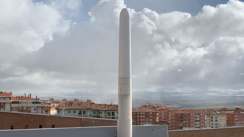 A bladeless wind turbine on a rooftop in a heavily populated area