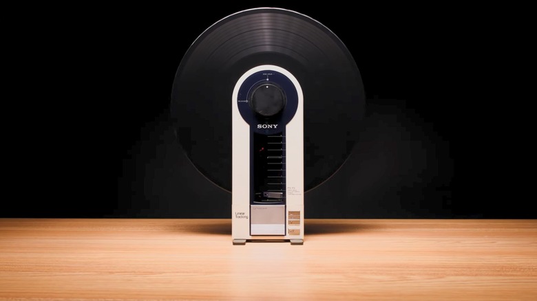 The Sony PS-F5 Flamingo vertical vinyl record player with a black record on a table in front of a black background