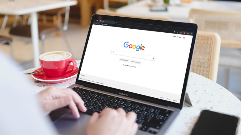 A behind-the-shoulder view of an individual using a MacBook to access Google Search through a web browser