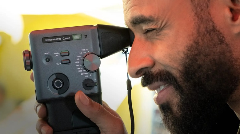 A man using the viewfinder on a Fujifilm insta mini Evo Cinema, the image highlights the features available on the side of the device, including the Eras Dial.