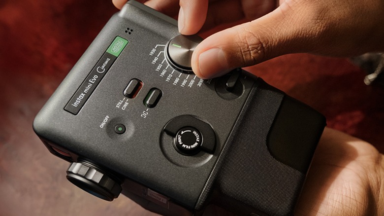 A closeup shot of the Fujifilm instax mini Evo Cinema, the right hand of an individual is adjusting the Eras Dial, which can set the device to a specific time in photography history.