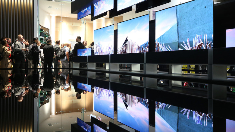Group of people standing near a display showcasing several OLED monitors or TVs.