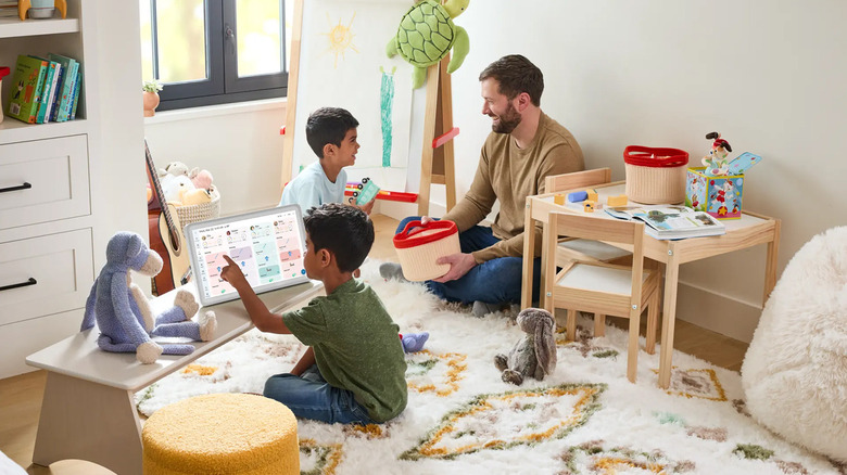 A father and two sons sitting in a playroom, one tapping on the Skylight Calendar.