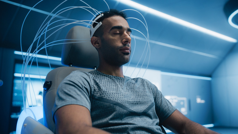 Man in a chair with a BCI setup connected to his head, reading his thoughts