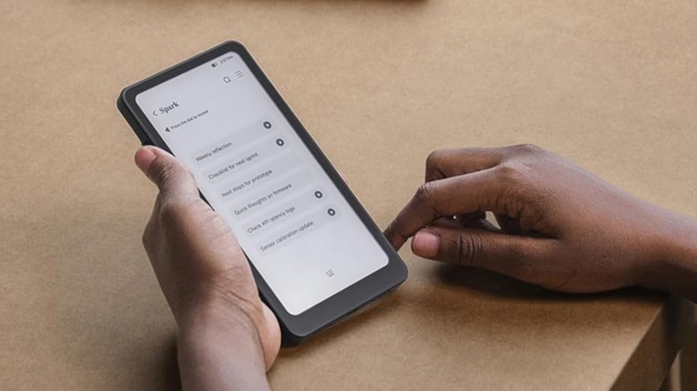 A closeup a black DoRuBo Krono held in a user's left hand, the device is displaying a chat with its AI assistant Spark