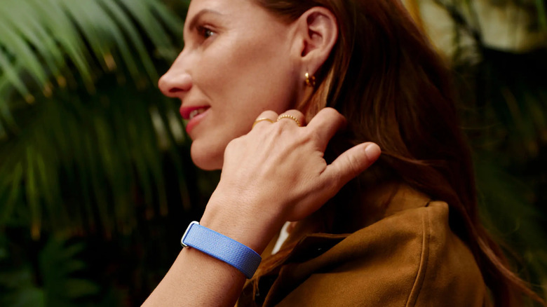 A woman wearing a blu Fitbit Air in front of a tropical background