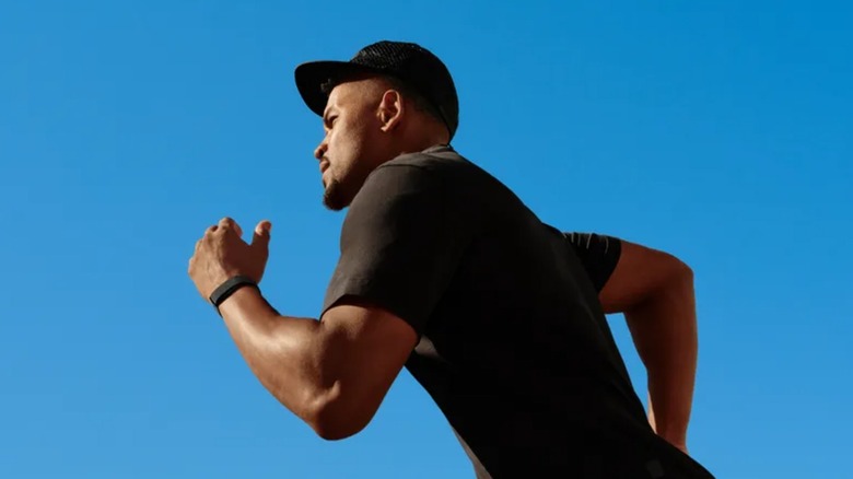 An individual in a black shirt and har appears to be running on a cloudless day, they are wearing a Google Fitbit Air on their left wrist
