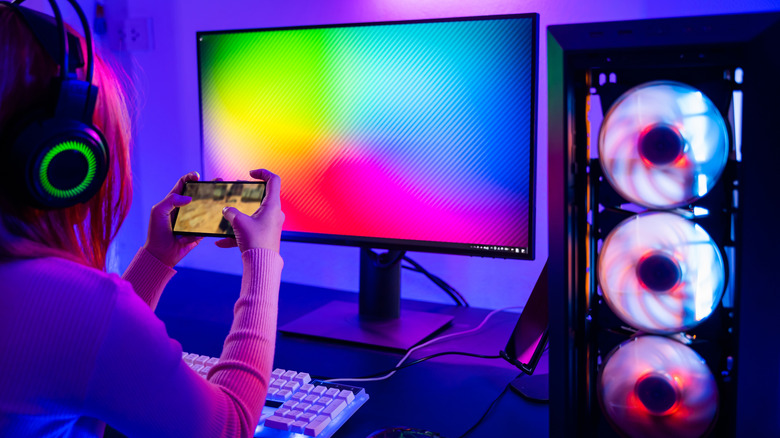 A person wearing a headset and gaming on their phone at a gaming computer.