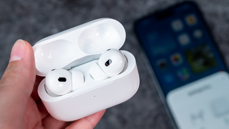 AirPods earbuds case open, with iphone showing airpods connected in background