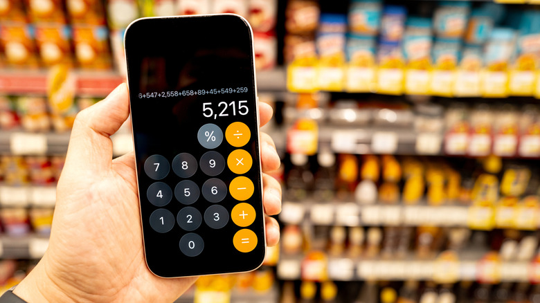 An individual holding an iPhone in their left hand, the device is displaying the phone's stock Calculator app