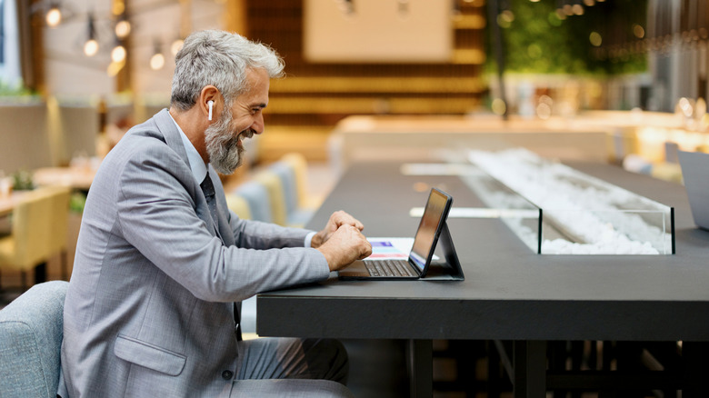 A man sitting up at a long table, wearing AirPods and working at a tablet