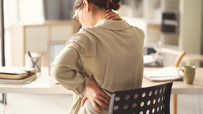 A woman sitting in a chair rubbing her back due to poor posture