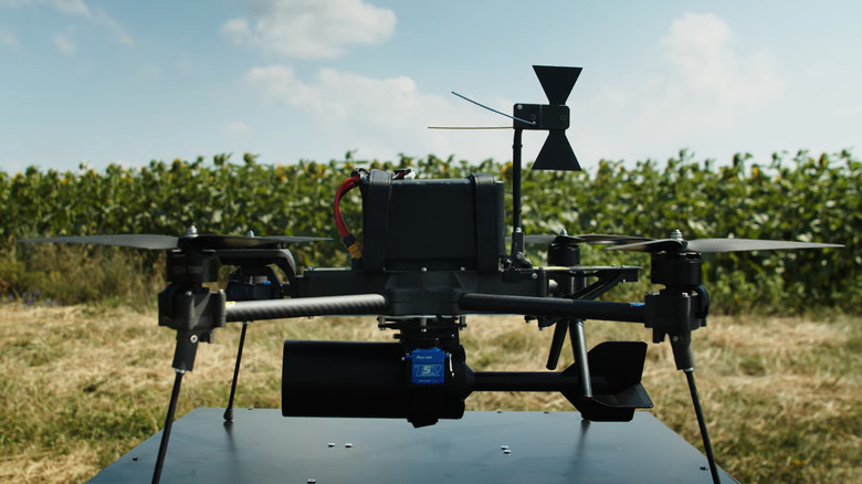 A black quadcopter Linza drone with a small explosive at its base resting on a launch pad in a field.