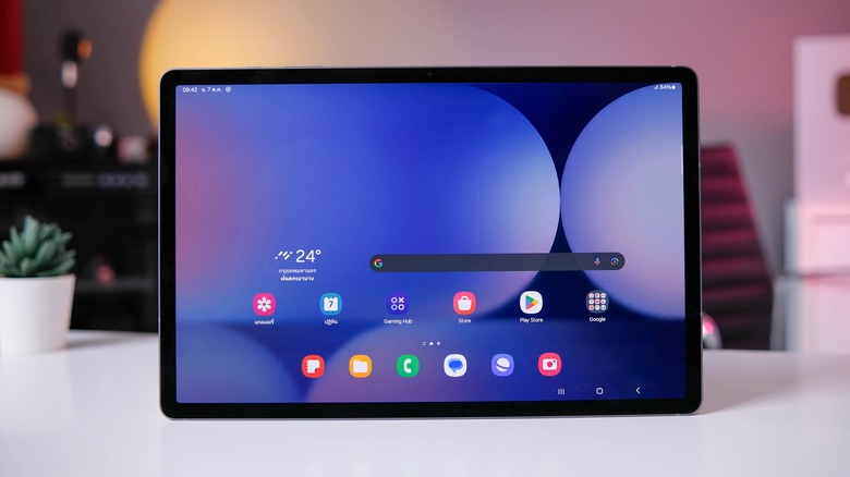 An Android tablet is perched on top of a table. The home screen shows several apps.