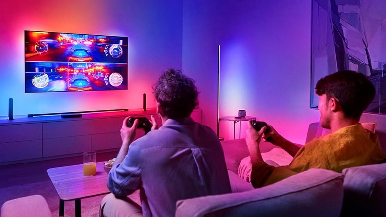 Two gamers using the Philips Hue Play HDMI Sync Box 8K. They play a racing game on a wall-mounted TV.