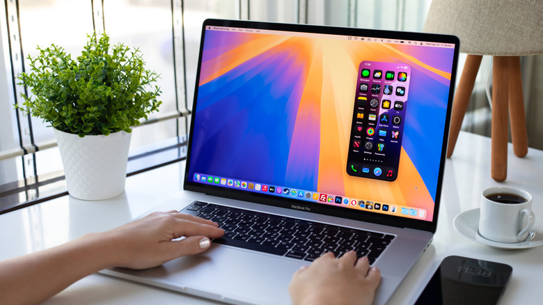 Close-up of a person using an Apple Macbook Pro on a white table with a plant and an iPhone on the side