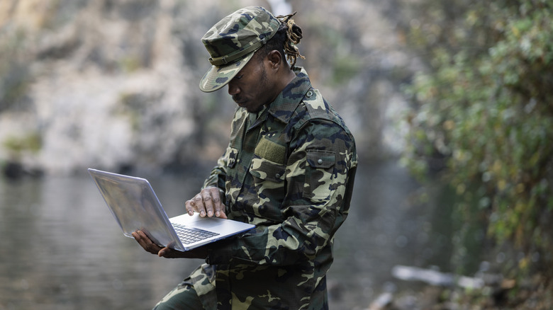 A male soldier consulting a laptop while in the field