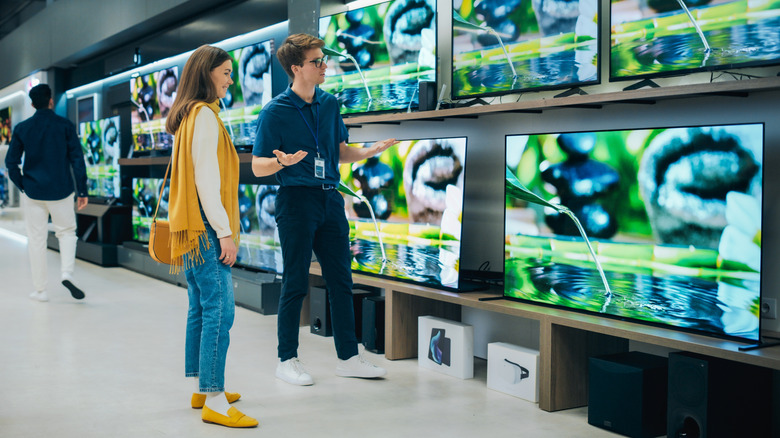 A woman consults with a store employee in the electronics section of a retail store