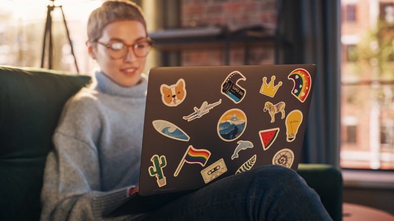 A person using a laptop adorned with stickers
