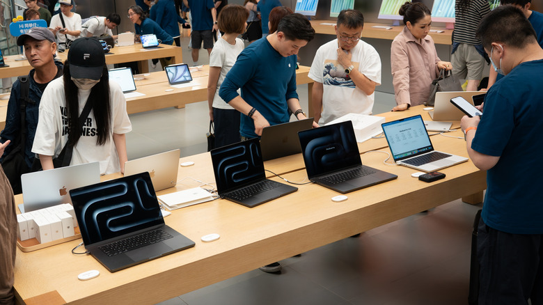 Customers around a table viewing and testing MacBook laptops at an Apple Store