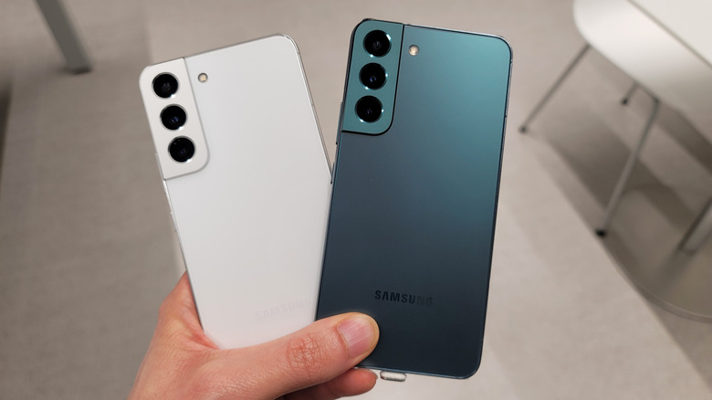 Samsung's Galaxy S22 series phones in white and green colors being held in a person's hand.