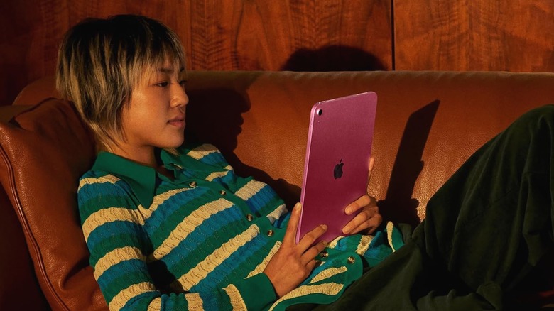 An individual in a striped sweater is laying down on the couch with an iPad in between their hands