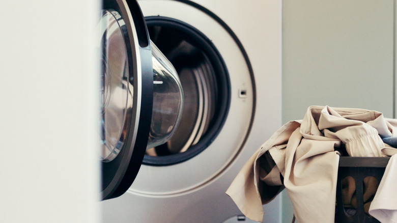 A load of dried laundry sits in a basket outside an open dryer on the floor of laundry room.