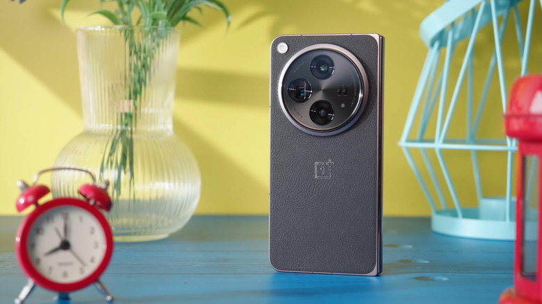 OnePlus Open standing a blue surface, showing the rear camera systems, with random household items in the frame