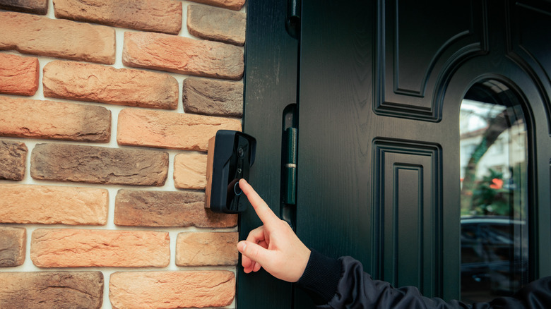 A person interacting with a video doorbell mounted to the exterior of a house.