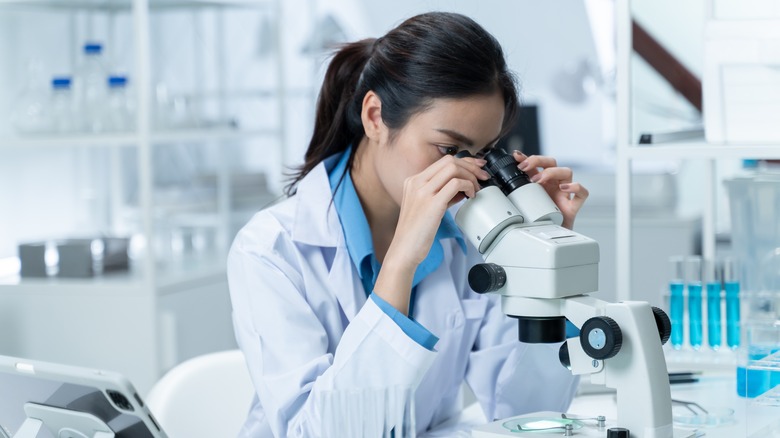 a female Asian scientist looking through a microscope in a lab