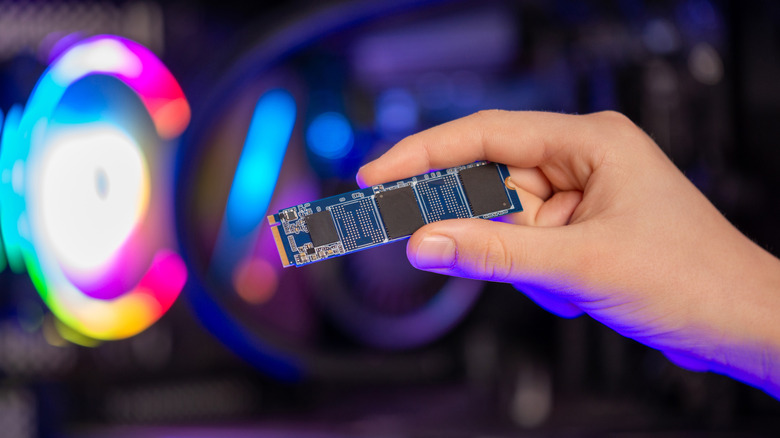 An M.2 NVMe SSD held in front of a desktop computer.