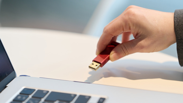 A red USB flash drive about to be plugged into a laptop