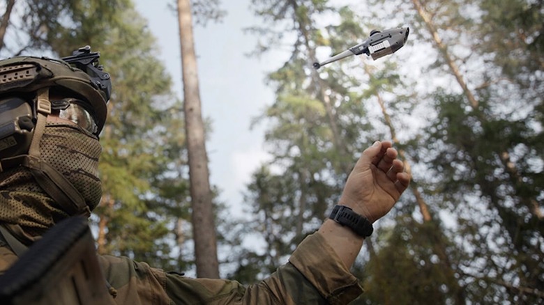 A soldier releases a Black Hornet drone in a forest.