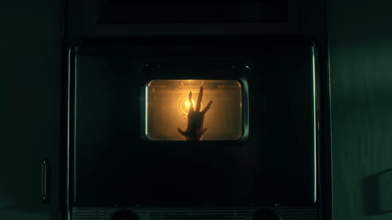 A monster-like hand seen resting inside a closed oven's glass