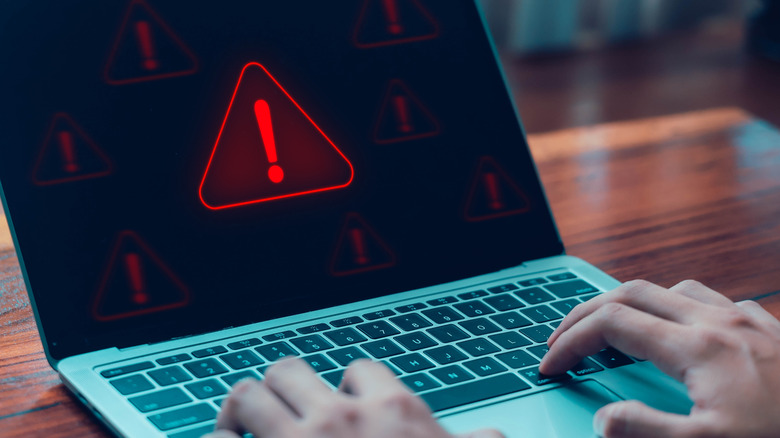 Image of a man at a laptop that has a warning symbol on it