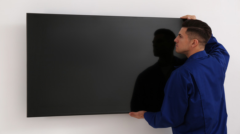 Technician mounting a TV flush against a blank wall.
