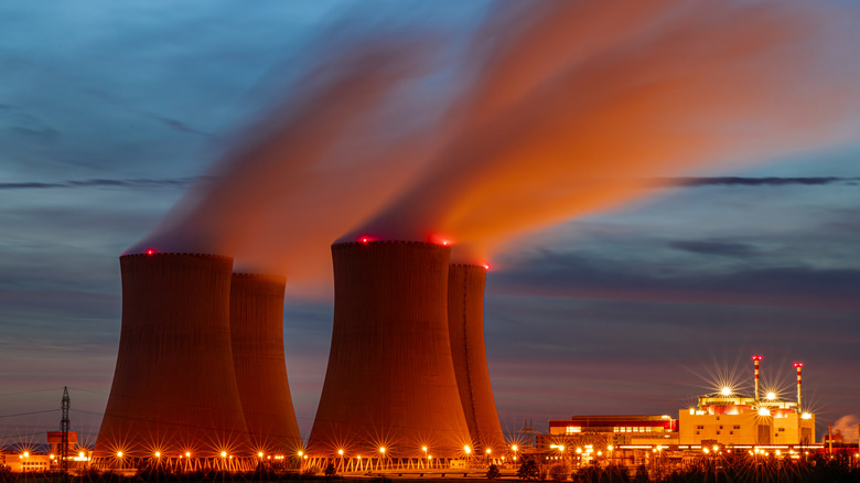 nuclear power facility with smoke rising out of the cooling towers, sunset sky in the background