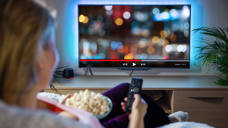 A woman with popcorn holding a TV remote in front of a TV.
