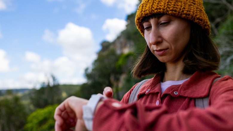 A woman in a hat outside looking at her smartwatch.