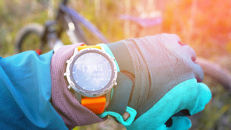 A hand on a bicycle showing a smartwatch screen.